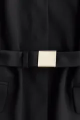 Blazer negro de botonadura simple con solapas de muesca, botones a presión ocultos adelante y cinturón extraíble con hebilla de metal. Modelo con hombreras, bolsillo insertado decorativo en el pecho y bolsillos delanteros ribeteados con solapa. Forrado.