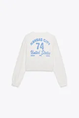 Sudadera corta color crudo de algodón, con cuello redondo, mangas largas y texto estampado en el frente que dice "IN MY YEEHAW ERA".