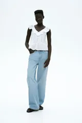 Blusa blanca sin mangas de tejido liviano de algodón con alforzas e inserciones de encaje, escote en V con ribete de volados y peplum con leve vuelo.