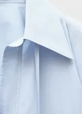 Camisa celeste de algodón, corte oversize, con cuello camisero, mangas largas con puños abotonados y cierre de lazo en el cuello.