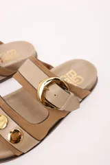 Sandalias bajas de cuero marrón con doble tira, hebilla ajustable y apliques de tachas metálicas.