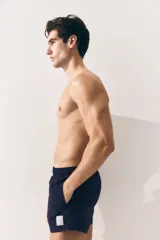 Short de baño azul marino de nylon con elástico revestido y cordón para ajustar oculto en la cintura, bolsillos laterales y bolsillo de solapa con cierre autoadherente atrás. Largo por encima de la rodilla con abertura corta en los laterales y suspensor interior en malla suave.