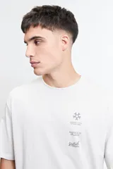 Remera blanca de manga corta con cuello redondo y corte oversize. Estampado frontal con textos y logos en gris.