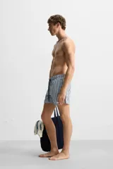 Bañador de hombre con rayas verticales azules y blancas, de corte medio, con cintura elástica ajustable con cordón, bolsillos laterales y trasero con solapa.