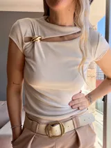 Remera beige de punto canalé con cuello redondo, manga corta y abertura en el pecho con broche dorado. Corte ajustado.