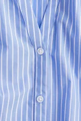 Blusa de popelina de algodón a rayas celestes y blancas, con cuello mao, abertura en V y botones frontales. Mangas globo tres cuartos de corte raglán con puños finos y bajo recto.