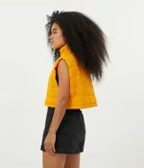 Chaleco cropped puffer color mostaza, con cuello alto y cierre frontal con cremallera.