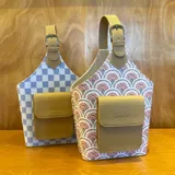 Bolso matero con diseño a cuadros color lila y blanco, con bolsillo frontal color beige y manija superior con hebilla.
