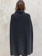 Poncho tejido de punto grueso color gris con cuello alto y aberturas laterales con ribete blanco.
