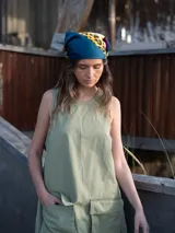 Vestido corto verde oliva, sin mangas, con cuello redondo y dos bolsillos grandes tipo parche en el frente.