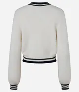 Cardigan corto de punto color crema con escote en V ribeteado en negro y blanco. Presenta cierre frontal de botones negros y puños con el mismo ribete a rayas. Las mangas son largas y ligeramente abullonadas.