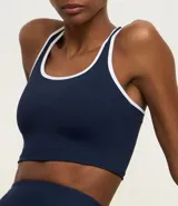 Top deportivo sin copa, color bordó, con escote en U y espalda tipo nadador. Presenta ribetes de color blanco en el contorno del escote y las sisas.