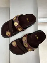 Sandalias marrones de cuero y gamuza, con apliques de monedas doradas.