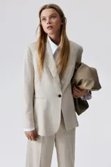 Blazer color beige de lino y viscosa, con solapas de pico, hombreras finas, cierre de un botón, pinzas en la cintura, abertura con botón en los puños, bolsillos delanteros ribeteados y abertura atrás.