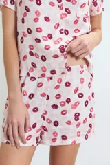 Pijama de dos piezas, compuesto por una camisa de manga corta con cuello y botones frontales, y un short. El conjunto es de color rosa pálido con un estampado repetitivo de labios en tonos rosados y burdeos.