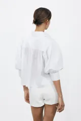 Camisa rosada de popelina de algodón, con cuello clásico, manga corta abullonada y cierre frontal con botones.