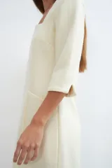 Vestido midi color crema con escote cuadrado, manga francesa con tajo y bolsillo lateral. Confeccionado en lana fina sin teñir.
