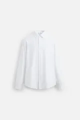 Camisa blanca de algodón, corte slim fit, cuello italiano, manga larga con puños abotonados y cierre frontal con botones.