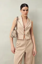 Chaleco sastrero color beige, con solapas clásicas y doble broche metálico frontal.
