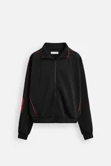Chaqueta negra con detalles en rojo, cuello alto, cierre frontal con cremallera, bolsillos laterales y puños elásticos.
