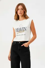 Remera blanca de algodón con cuello redondo y mangas cortas con hombreras. Estampado frontal con la frase "Heaven Made" en azul y dorado.
