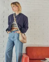 Bandolera color beige con textura símil reptil, cierre con broche metálico dorado y correa larga regulable.