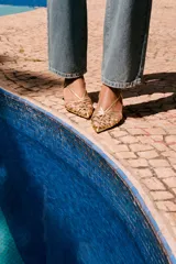 Zapato destalonado dorado con tiras finas entrecruzadas en la parte delantera, cierre con hebilla ajustable en la tira trasera, tacón fino alto y acabado en punta. Altura del tacón: 6 cm.