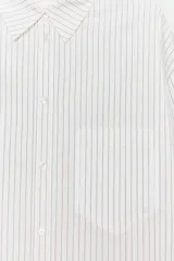 Camisa blanca con finas rayas verticales negras, de corte holgado, cuello solapa, manga larga con puños y bolsillo de plastrón en el pecho.