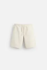 Bermuda color beige de denim de algodón, corte relaxed fit, con cintura elástica ajustable con cordón, bolsillos frontales y traseros.