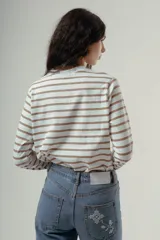 Camiseta de manga larga con cuello redondo, confeccionada en algodón, con un patrón de rayas horizontales blancas y marrones. Presenta un pequeño logo bordado en color rojo en el pecho.
