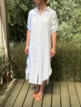 Vestido camisero largo de lino blanco, con corte en la cintura, abertura lateral y botones de nácar.