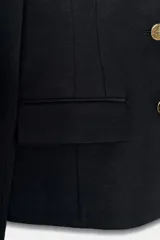 Blazer corta de color negro, entallada, sin solapa y con escote en V. Posee hombreras, cierre frontal de tres botones dorados y dos bolsillos delanteros con solapa.