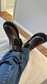 Botas de cuero color marrón oscuro, estilo Chelsea, con elástico lateral negro y suela track negra. Incluye correa de cuero desmontable con hebilla.