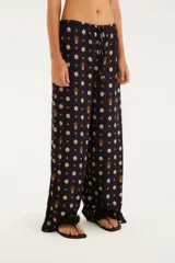 Pantalón negro con estampado de flores y piñas, corte holgado, tiro medio con elástico en la cintura y ruedo con volados.