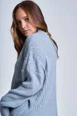 Sweater color crema de punto trenzado, con cuello alto y mangas largas.