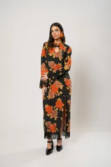Vestido largo negro con estampado de flores naranjas y amarillas, cuello mao con abertura en forma de gota, mangas largas acampanadas con botones en los puños, tajo lateral y flecos en el ruedo.