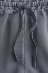 Short gris de felpa de algodón con efecto lavado, corte holgado, cintura elástica con cordón ajustable, bolsillos laterales y traseros, y aberturas laterales en el ruedo.