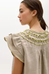 Vestido corto celeste de lino, corte suelto, con cuello redondo con volados y lazo, mangas cortas con volados.