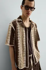 Camisa de hombre de corte relajado, confeccionada en tejido de crochet con estructura abierta. Presenta cuello bowling, manga corta y cierre frontal con botones.