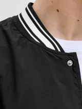 Campera bomber negra con cuello tipo baseball y puños de canalé. Cierre frontal con botones a presión y bolsillos laterales.