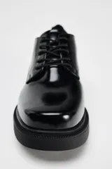Zapato tipo mocasín negro acharolado con punta redonda y cierre de cordones. Suela de 4 cm de altura.