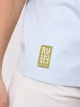 Remera negra de algodón con corte holgado y estampado frontal con el texto "Rusty Australia Mermaid Beach" en colores naranja, verde y amarillo.