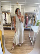 Vestido largo sin mangas, color marrón oscuro, con escote en V y corte amplio que cae hasta el tobillo. El ruedo tiene un acabado deshilachado.