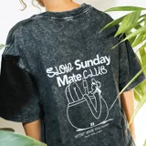 Remera negra con efecto acid wash y estampa en la espalda con la frase 'Slow Sunday Mate Club' y un dibujo de una persona tomando mate.