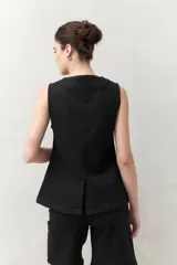 Chaleco sastrero negro sin mangas, con cuello redondo, botones metálicos frontales a presión y bolsillos ojal en la parte inferior.