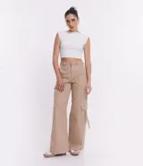 Pantalón cargo de sarga color beige, corte sastrero, con cintura alta, trabillas, cierre con botón y cremallera, y bolsillos laterales tipo cargo.