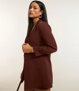 Blazer sastre femenino confeccionado en crepé color marrón, de modelo oversized y comprimento alargado. Sin estampa, posee bolsillos y detalle de pliegues en los puños.