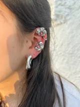 Par de aros plateados con forma de flor y centro de cristal rosado. Uno de los aros es un cuff que se engancha en el cartílago superior de la oreja y se une al aro inferior con una cadena de bolitas.