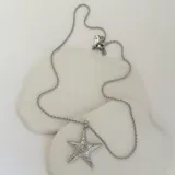 Collar con cadena plateada y dije de estrella de mar con diseño texturizado y espiral en el centro.