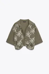 Camisa corta color verde oliva con bordado de hojas blancas, cuello solapa, escote pico y manga corta con vuelta.
